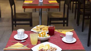 Ein Essbereich mit Tischen, die für das Frühstück gedeckt sind, darunter Teller mit Eiern, Speck und Bohnen sowie Tassen Kaffee und Saft.