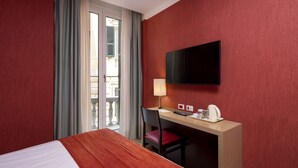 Hotelkamer met een bed, bureau met stoel, televisie, lamp en raam met gordijnen.