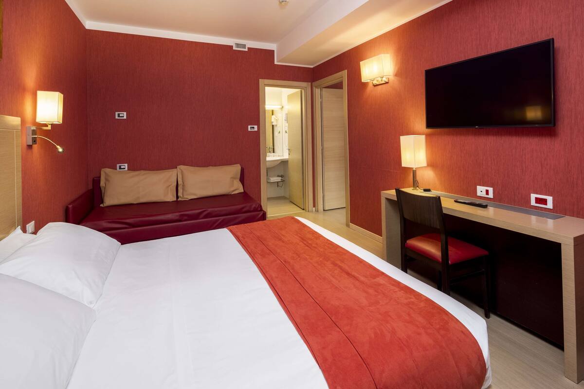 A hotel room with a large bed, a desk with a chair, a television, and a mirror.