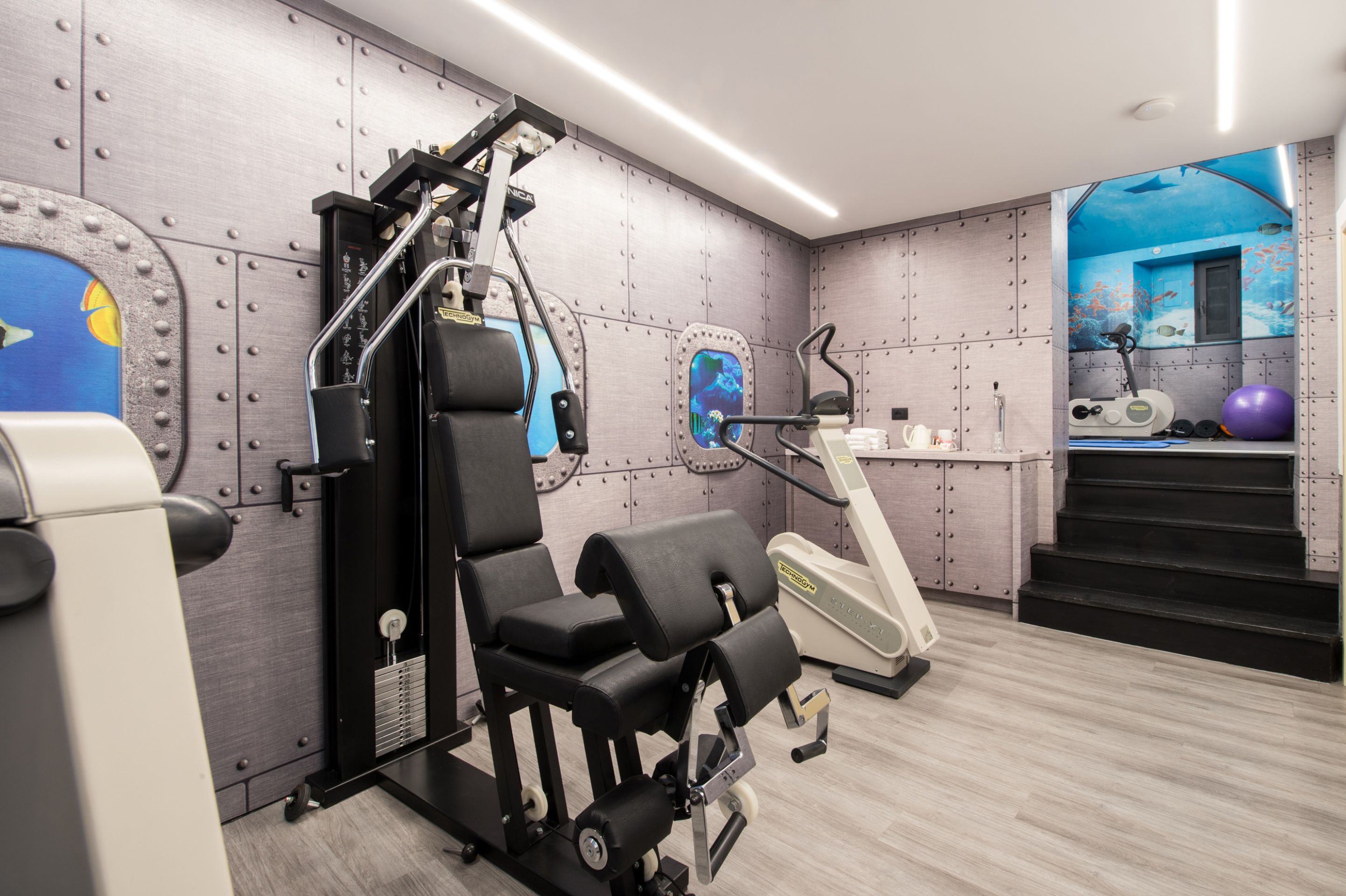 A modern gym with exercise equipment, a wall mural, and a staircase.
