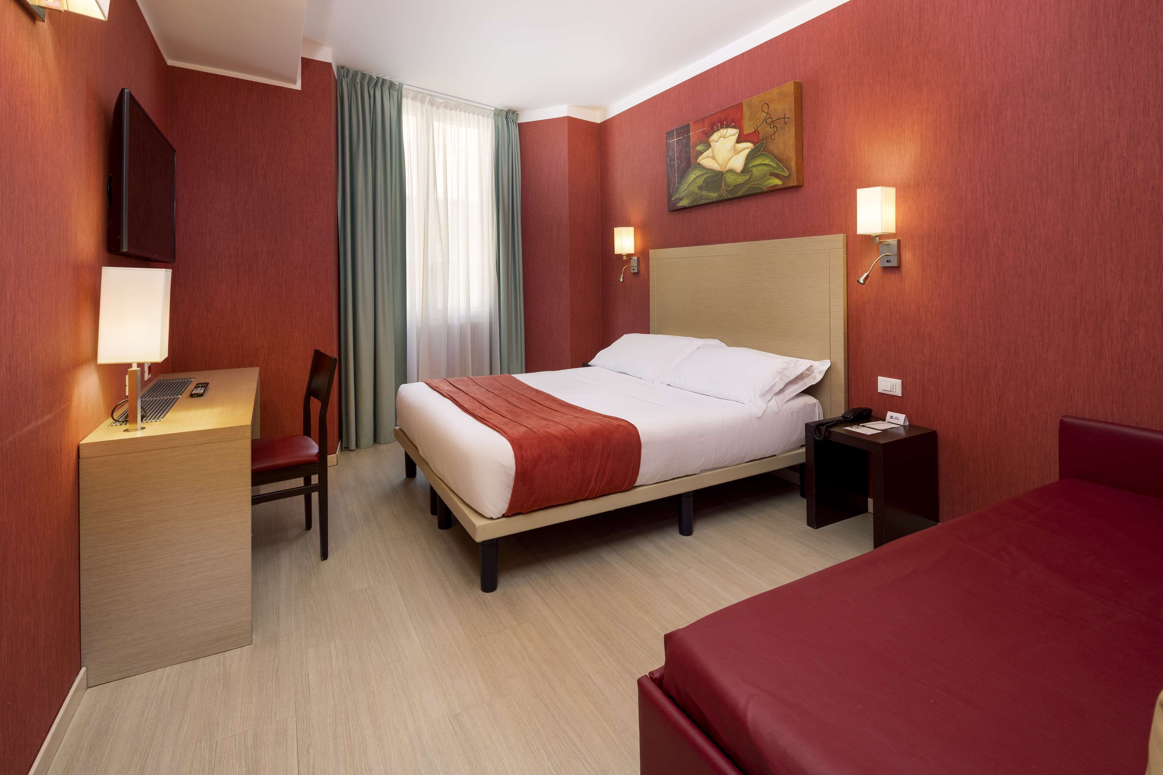 Ein Hotelzimmer mit Bett, Schreibtisch, Stuhl, Fernseher und einem Bild an der Wand.