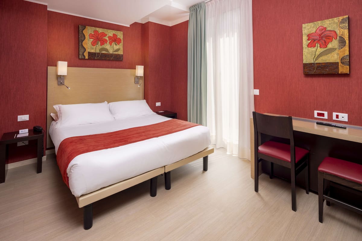 A hotel room with a large bed, a desk, and two chairs.