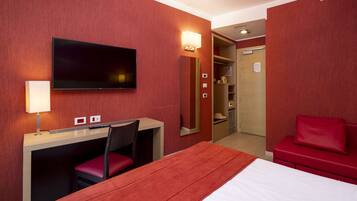 A hotel room with a bed, a desk with a chair, a TV, a red couch, and a mirror.