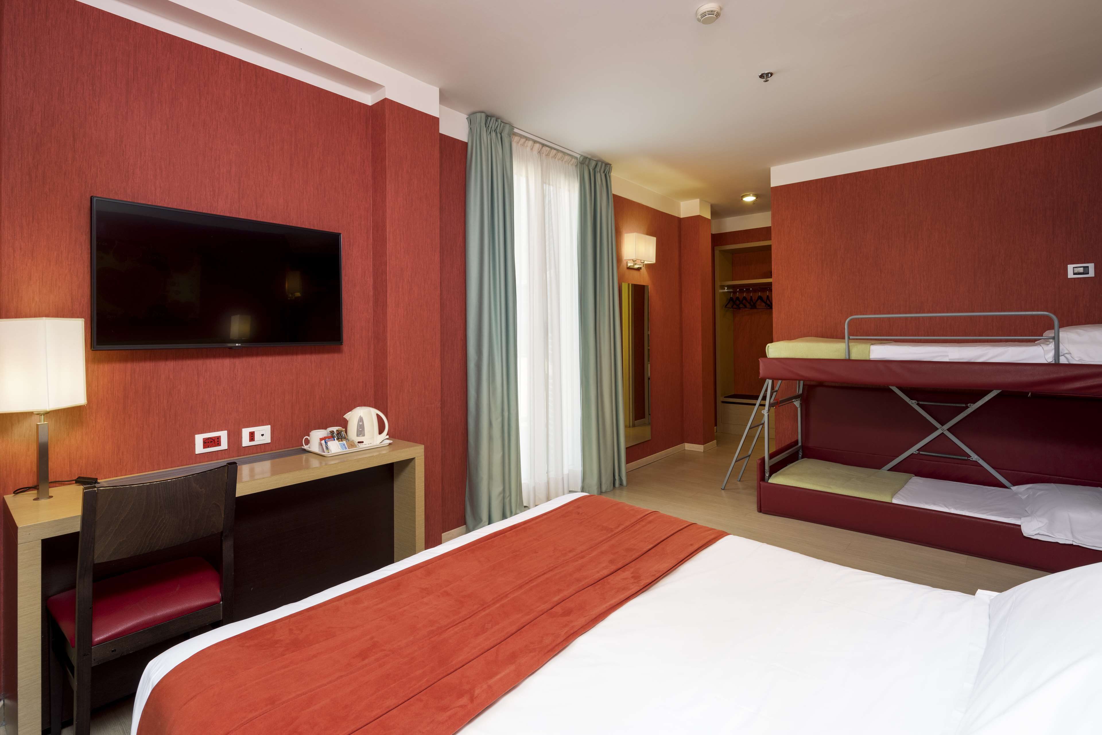 Een hotelkamer met een groot bed, een bureau met stoel, een aan de muur bevestigde televisie en een stapelbed.