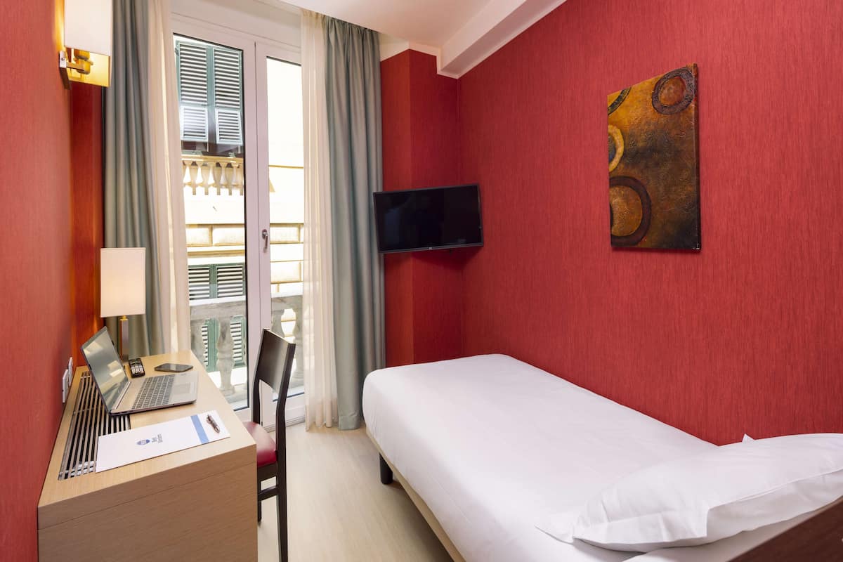 A hotel room with a bed, desk, chair, and a TV mounted on the wall.