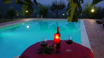 A poolside table with a red tablecloth, two wine glasses, and a bottle of wine.