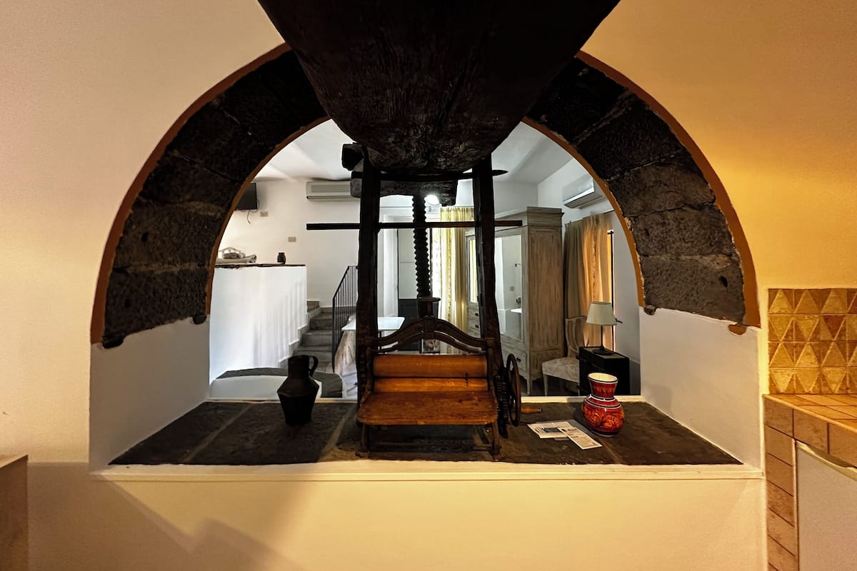 A narrow passageway with an arched ceiling, a wooden bench, a red vase, and a small table with papers.