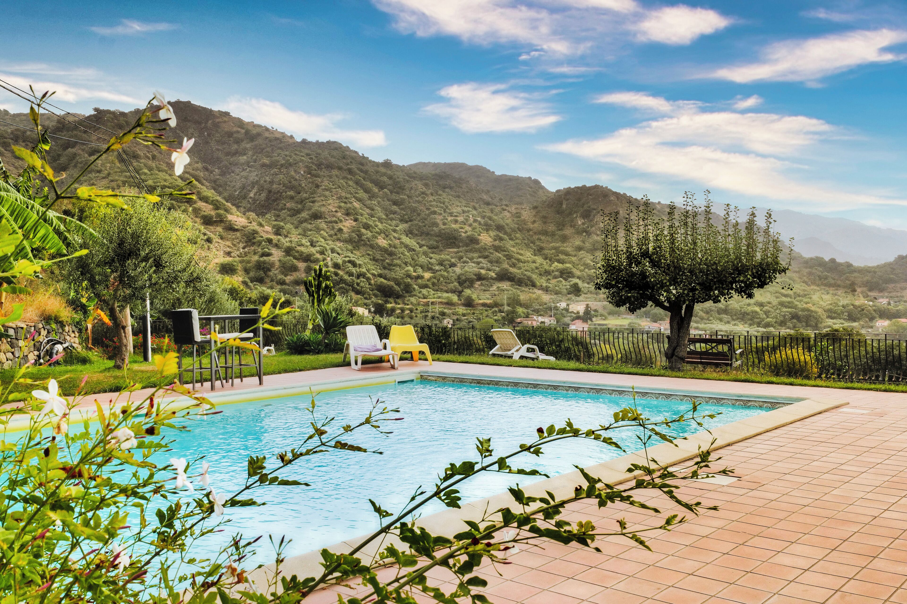 Une piscine avec vue sur les montagnes, entourée de verdure et dotée d’un espace extérieur aménagé pour se détendre.