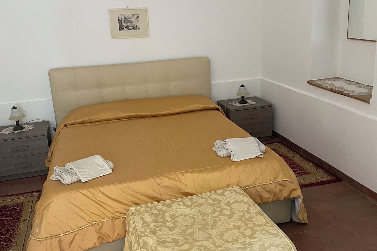 A bedroom with a bed, a nightstand, a bedside table, a mirror, and a rug.