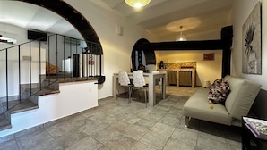 A spacious living area with a staircase, a dining table with chairs, a sofa, and a kitchen area. - Casale Romano Resort (Motta Camastra)