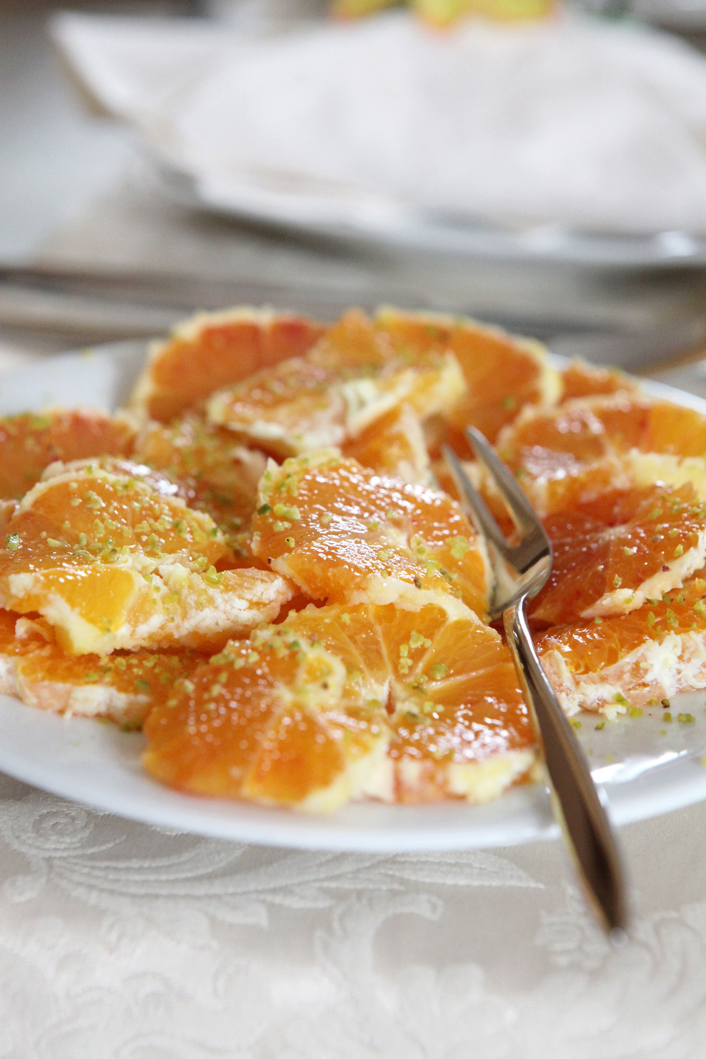 Un plato de rodajas de naranja adornado con ralladura verde, con un tenedor al lado.