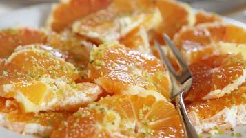 Un plato de rodajas de naranja adornado con ralladura verde, con un tenedor al lado.
