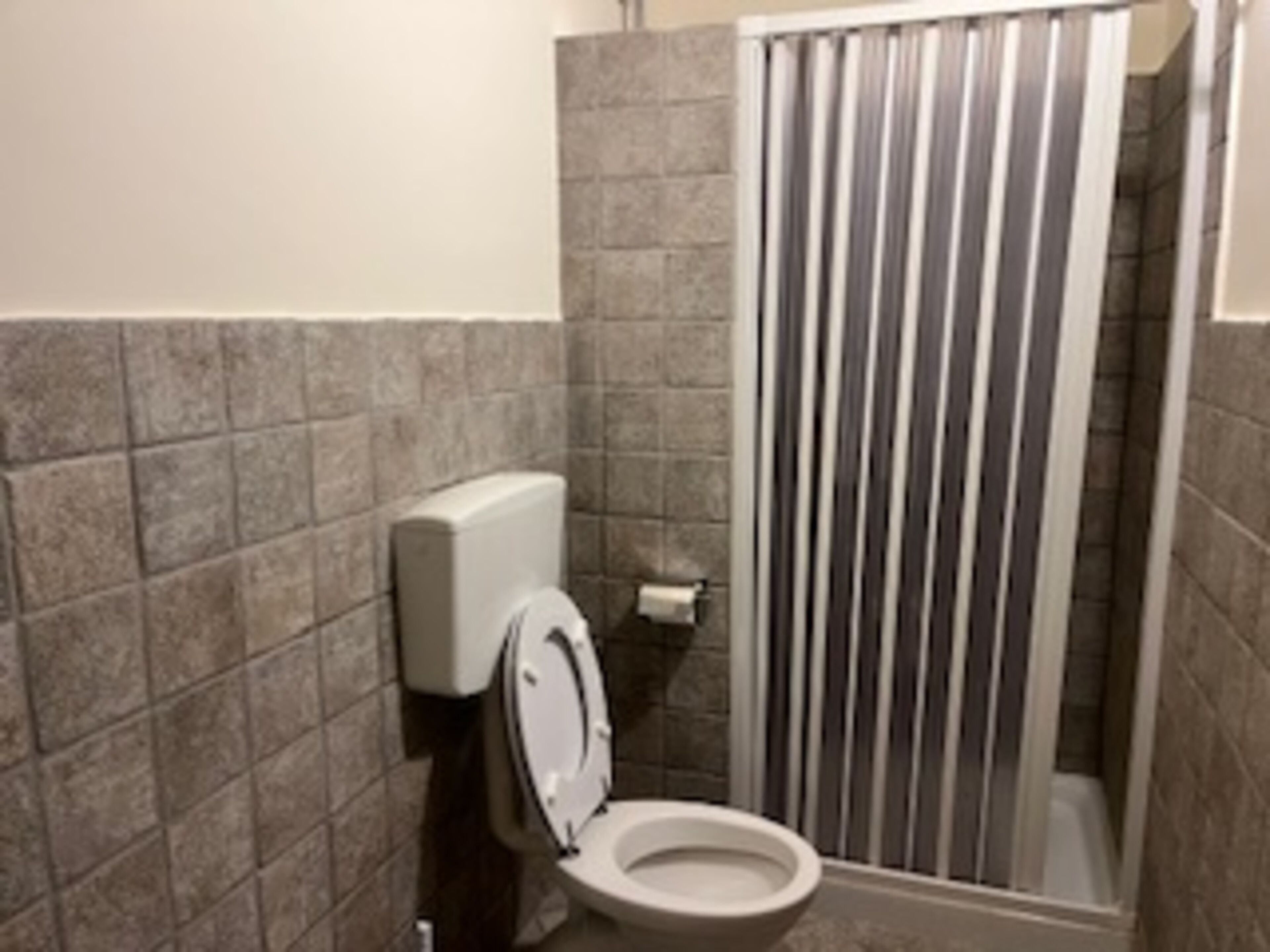 Une salle de bain équipée de toilettes, d’une douche avec des stores verticaux et d’un distributeur de papier toilette.