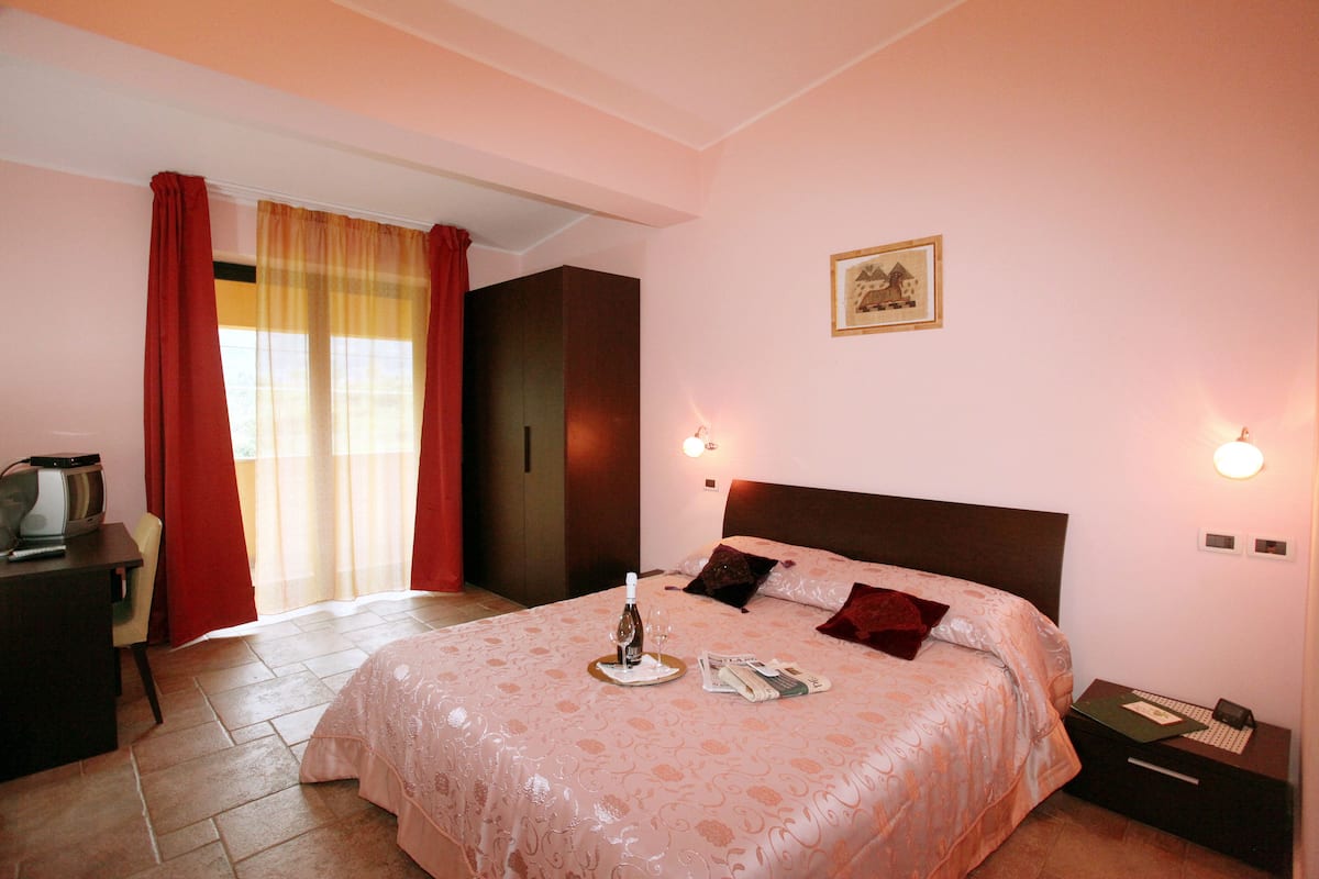 A hotel room with a bed, a desk, a chair, a wardrobe, and a window with curtains.