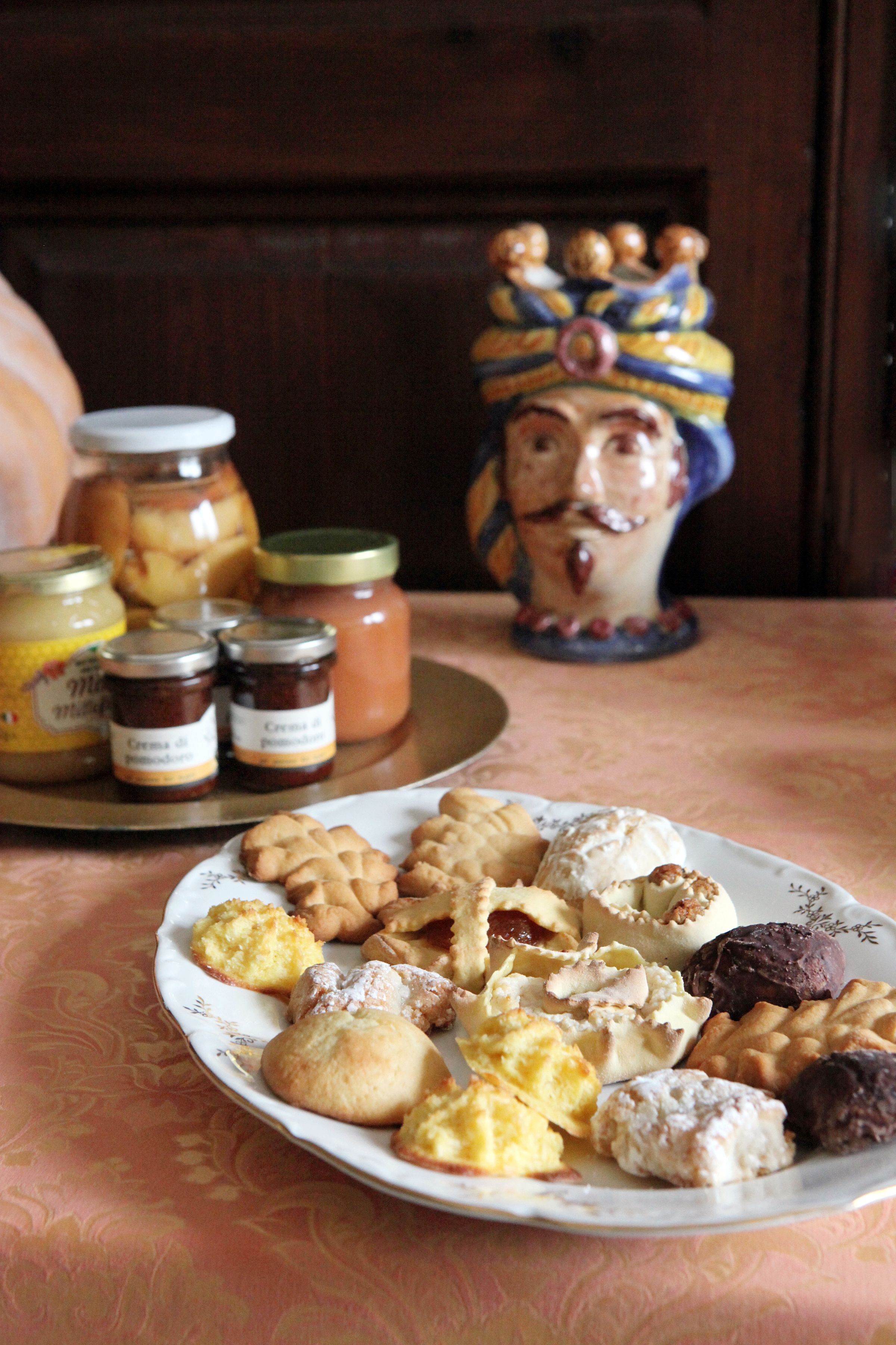 Een bord met diverse gebakjes en potten jam op een tafel met een geruit tafelkleed.