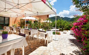 Une terrasse extérieure avec des tables et des chaises, entourée de plantes et de fleurs en pot, et offrant une vue sur les montagnes en arrière-plan.