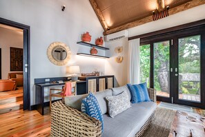 A cozy living room with a grey sofa, wicker chair, and a wooden coffee table. There are shelves with decorative items and a large mirror on the wall.