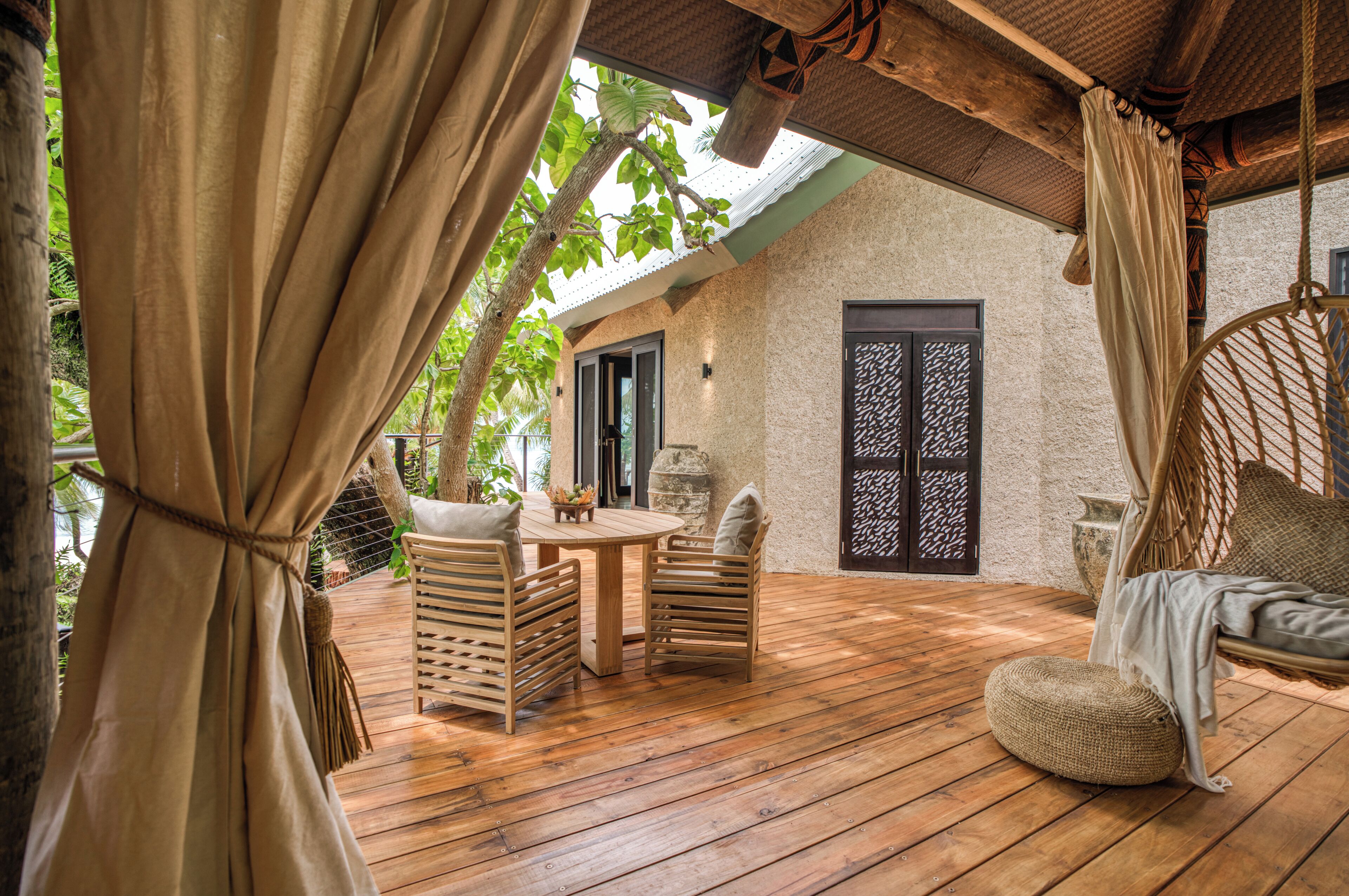Una terraza de madera con una mesa redonda y sillas, un columpio colgante y una puerta con un panel decorativo.