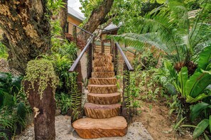A wooden staircase surrounded by lush greenery, leading up to a building with a metal railing.