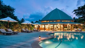 A resort with a swimming pool, lounge chairs, umbrellas, and a building with a dome roof. - Matangi Island Resort - Adults Only (Matangi Island)