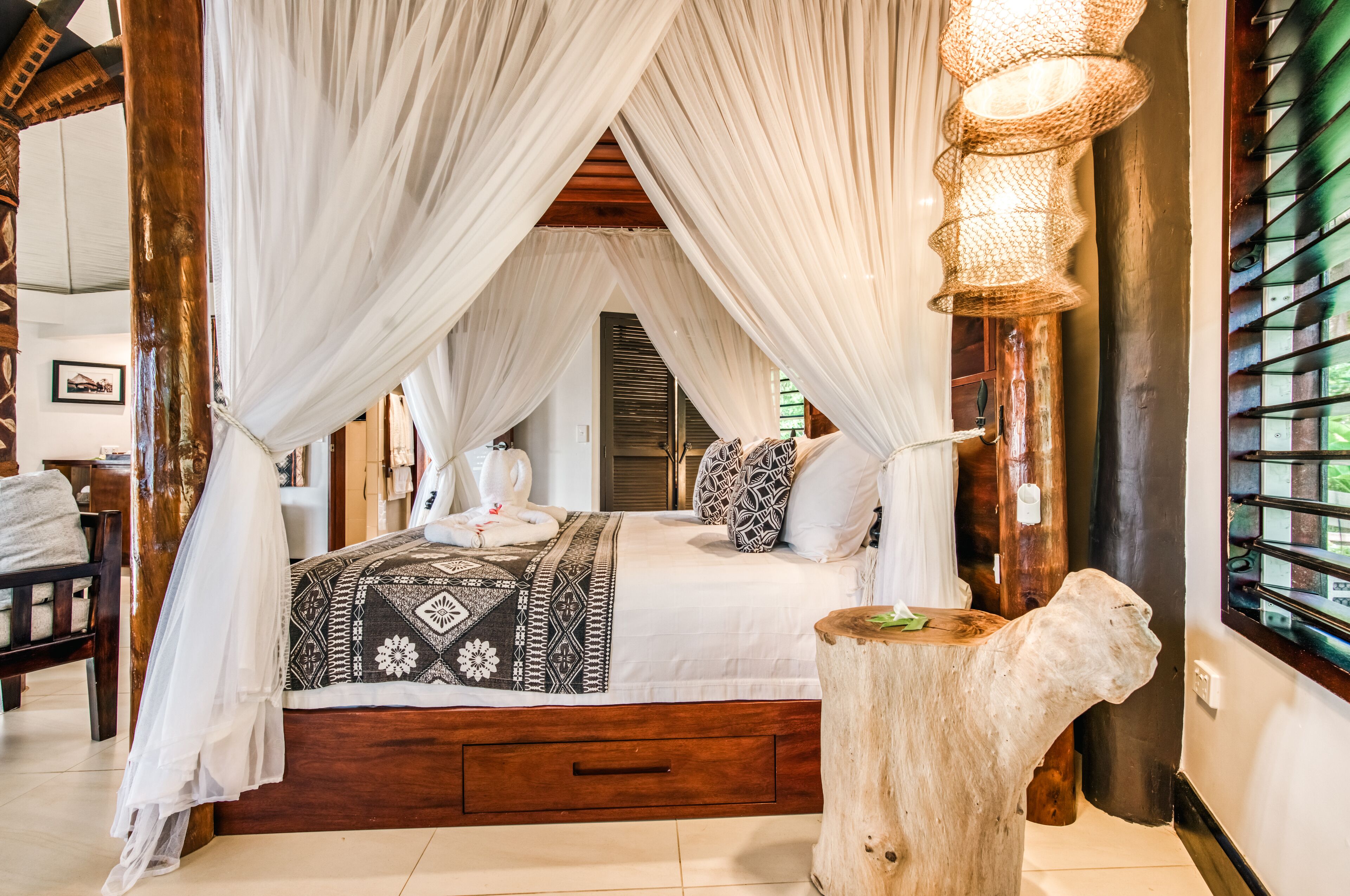 A bed with a canopy, a wooden nightstand, and a large window with a view.