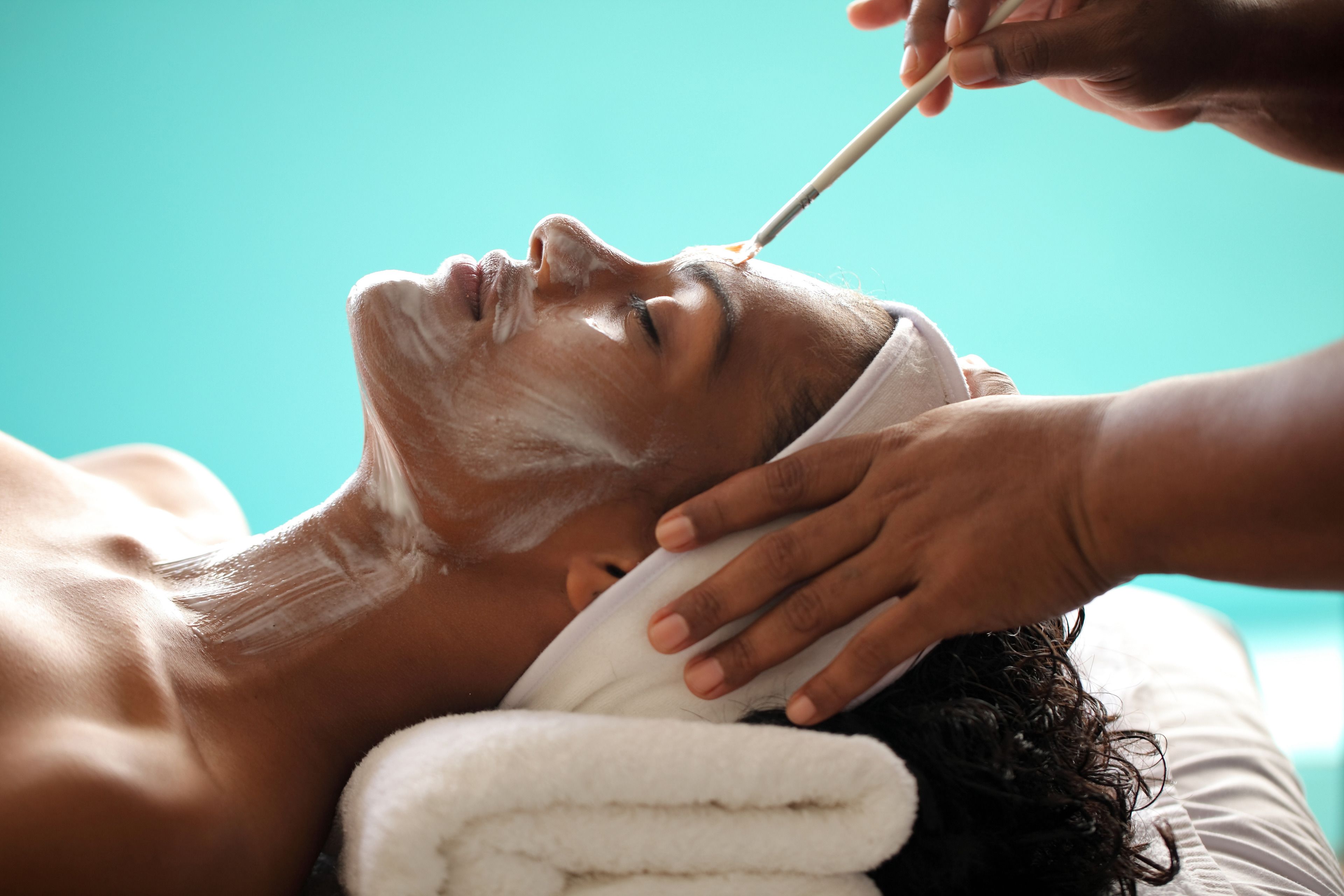 Une personne allongée, la tête enveloppée d’une serviette, en train de recevoir un soin du visage.