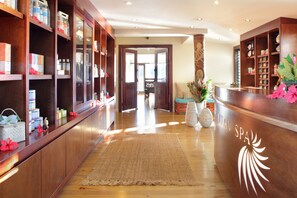 A reception area with wooden shelving displaying various items, a reception desk with a logo, and a large woven rug on the floor.