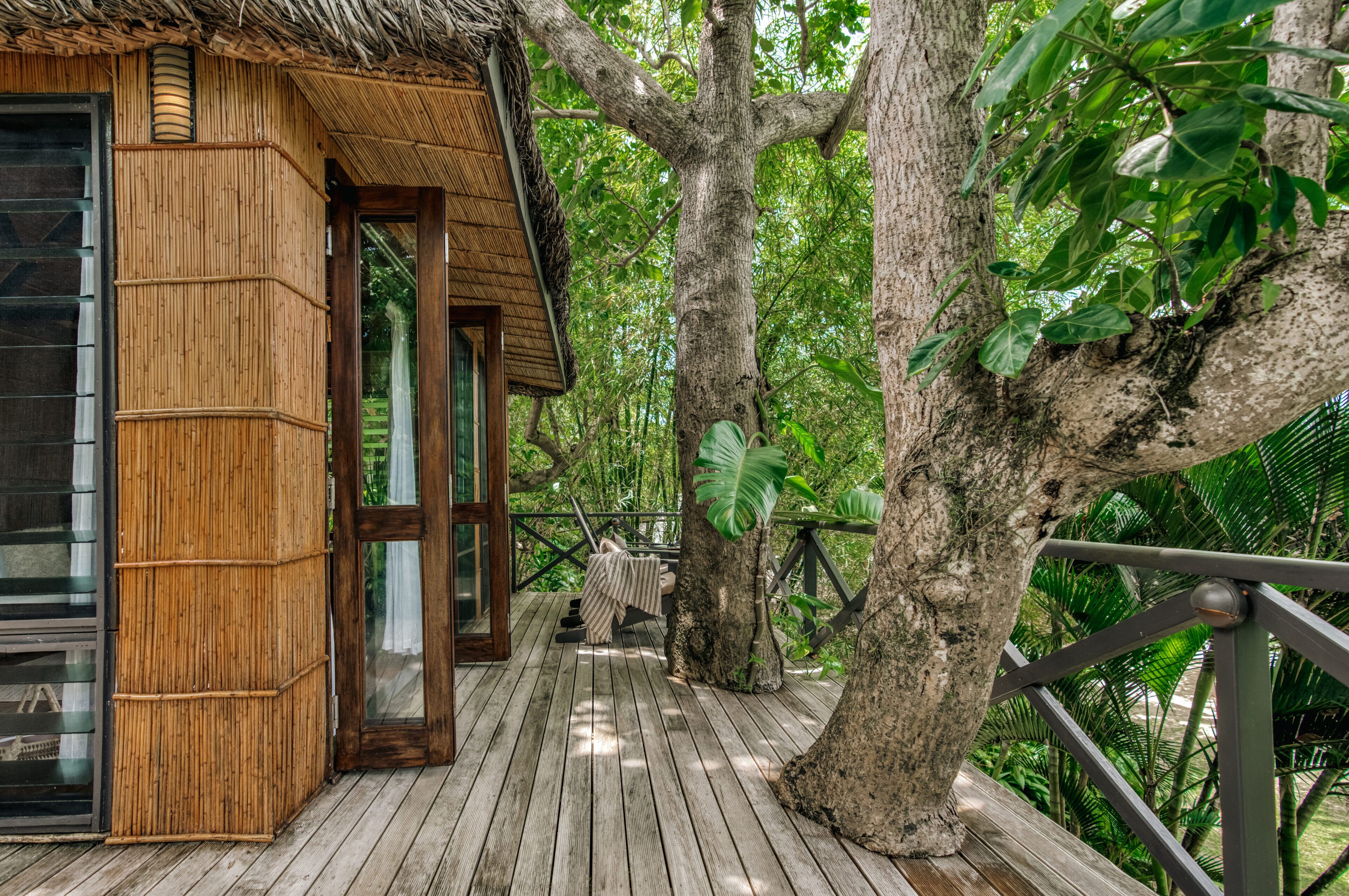 A wooden deck with a thatched roof structure, surrounded by lush greenery and trees.