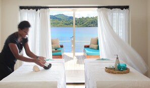 A room with two beds, a view of a lake, and a person arranging items on a table.