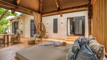 A spacious bedroom with a large bed, a wooden deck, wicker furniture, and a stone wall.