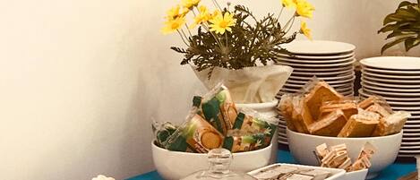 Una mesa de buffet con diversos alimentos, como pan, pasteles y un arreglo floral.