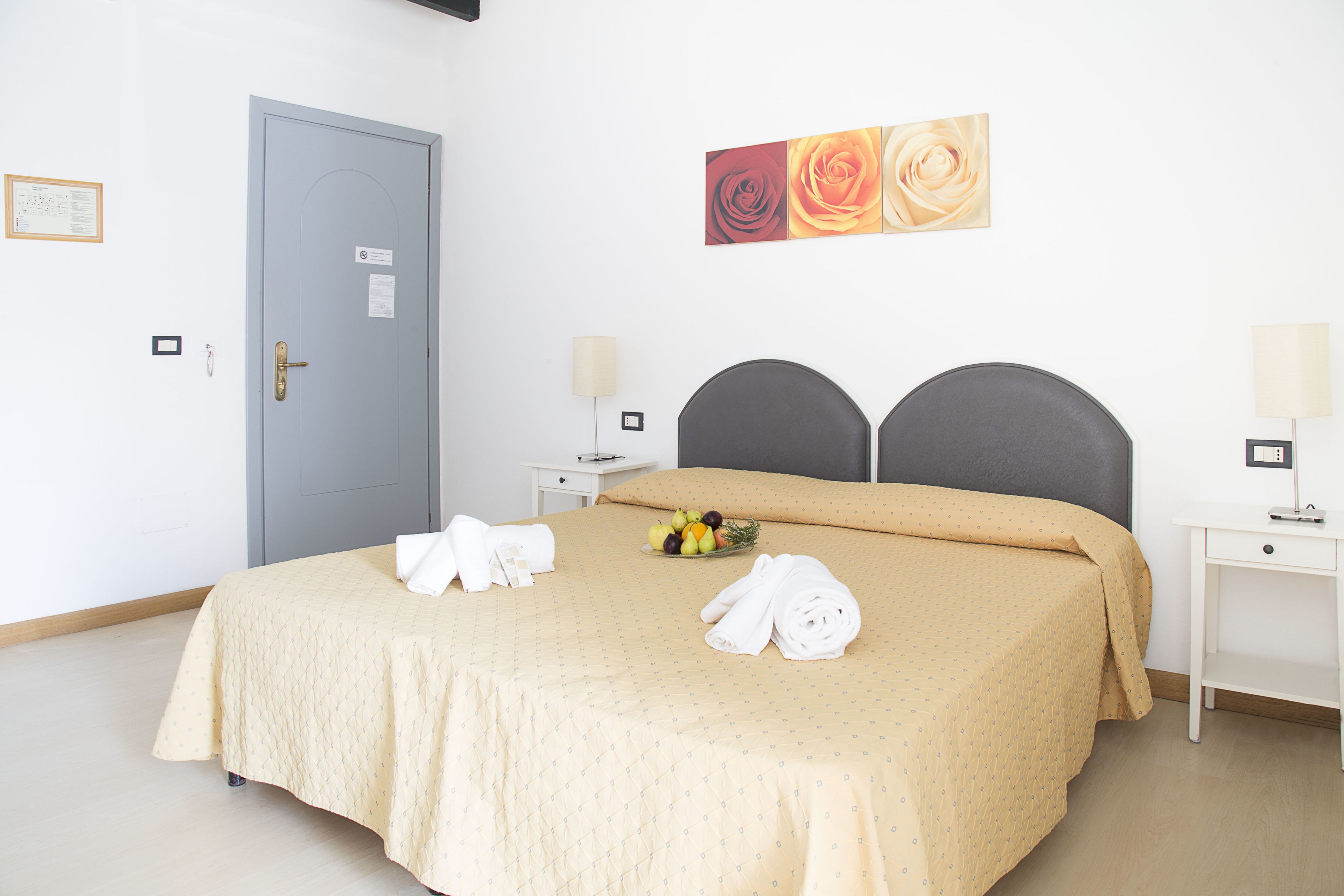 Une chambre d’hôtel avec un lit, deux tables de chevet, une porte et un tableau représentant des fleurs accroché au mur.