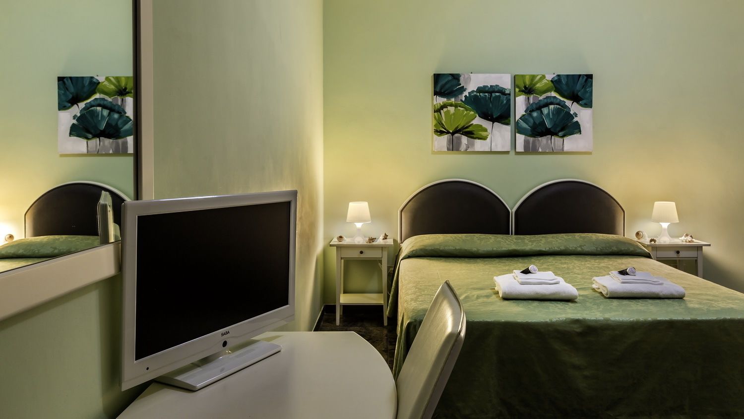 Une chambre d’hôtel avec deux lits, un téléviseur à écran plat, des lampes de chevet et des œuvres d’art accrochées aux murs.