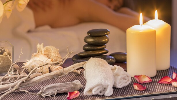 A massage therapy room with a person receiving a back massage, candles, and spa amenities like stones and towels. - Hotel Cala di Seta (Calasetta)