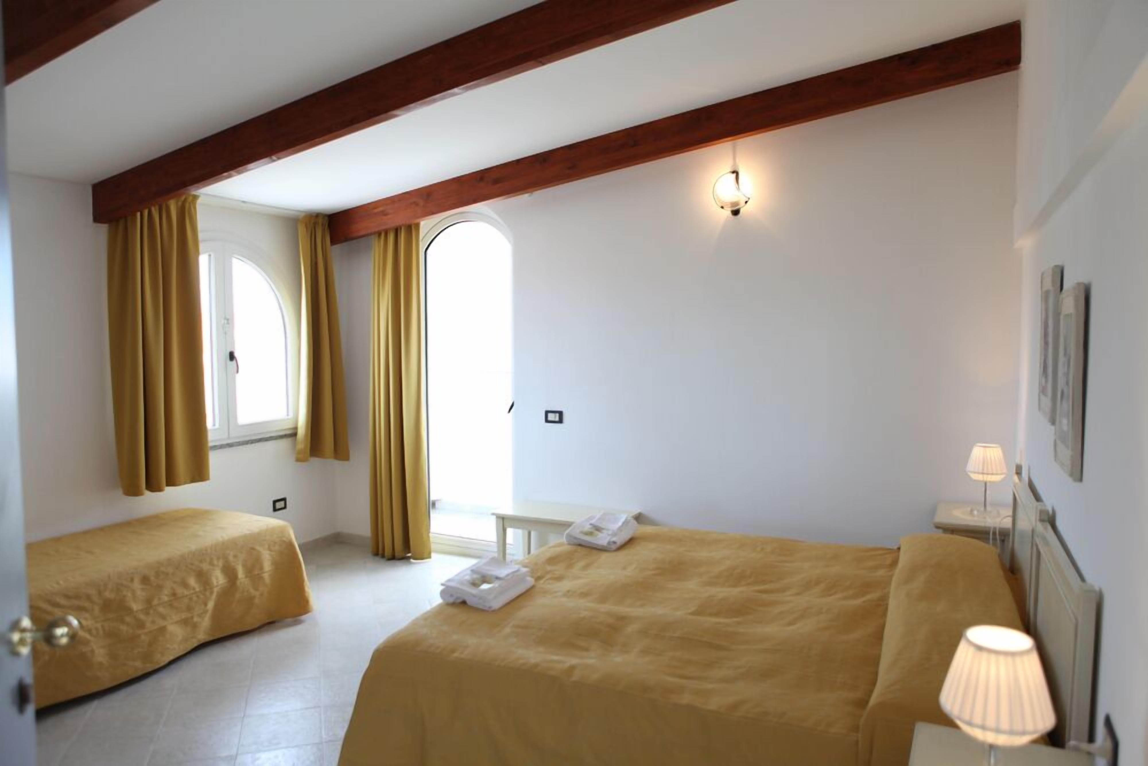 A hotel room with two beds, a window with curtains, a bedside lamp, and a small table.