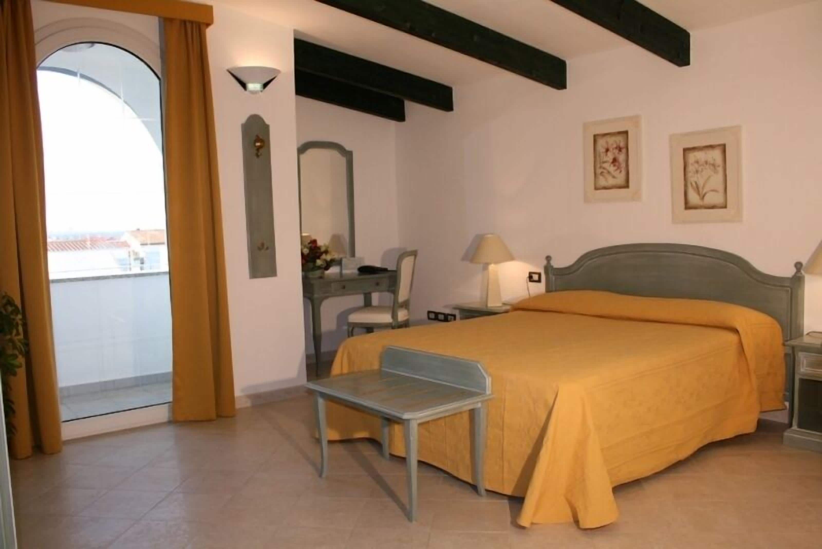 A bedroom with a bed, a chair, a desk, a mirror, and a nightstand.