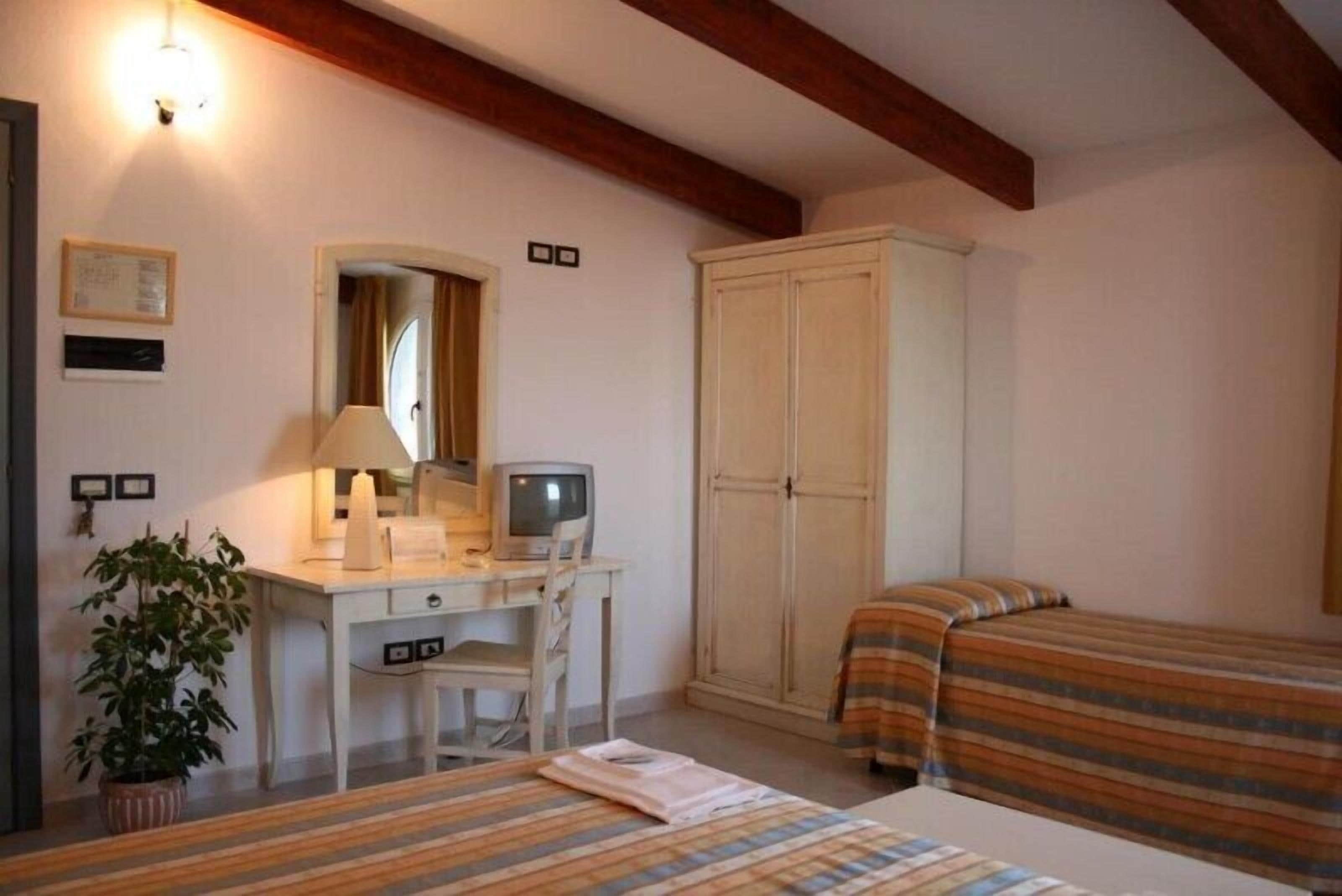 A bedroom with a desk, a television, a wardrobe, two beds, and a potted plant.