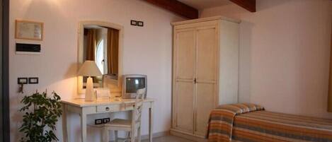A bedroom with a desk, a television, a wardrobe, two beds, and a potted plant.
