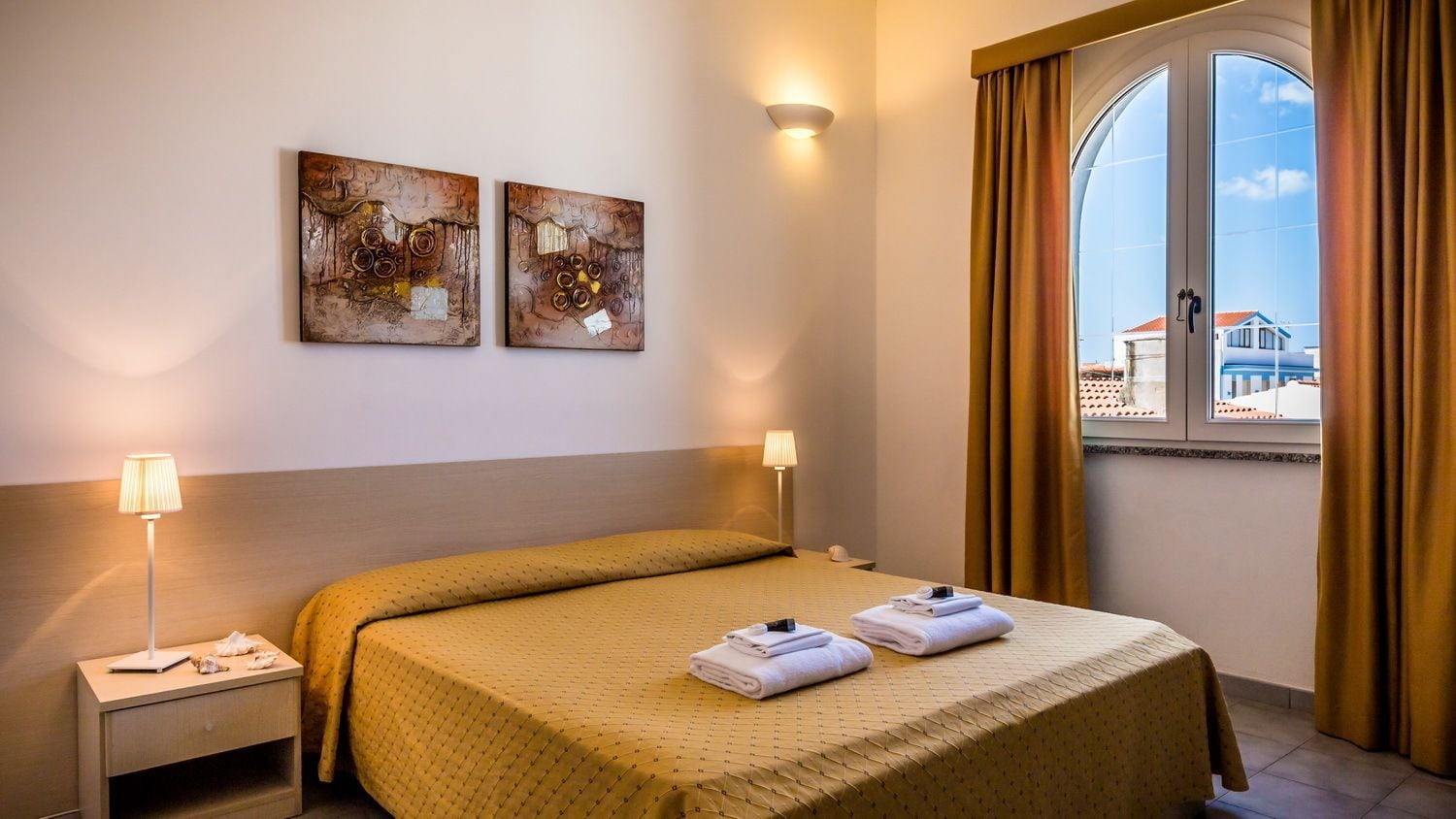 A hotel room with a bed, two wall-mounted lamps, and two abstract paintings.