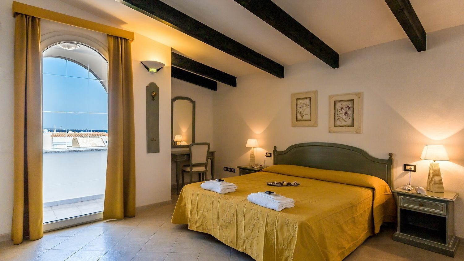 A hotel room with a bed, a desk, a chair, a nightstand, and a view through a large window.
