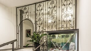 A modern interior with a staircase featuring ornate metal railings and a glass railing on the upper level. - Hotel Cala di Seta (Calasetta)