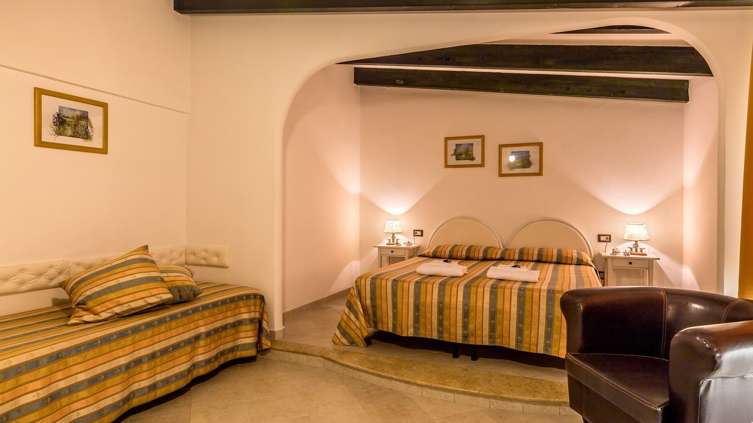 Una habitación de hotel con una cama, un sofá, una silla y dos mesitas de noche con lámparas.