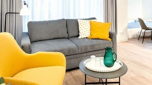 Una sala moderna con un sofá gris, un sillón amarillo y una mesa redonda de centro con un jarrón verde y saleros y pimenteros.
