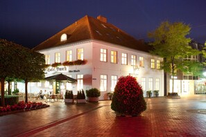 A hotel with a traditional European architectural style, featuring a symmetrical facade, multiple windows, and a well-lit entrance area with outdoor seating. - Hotel Busch (Westerstede)