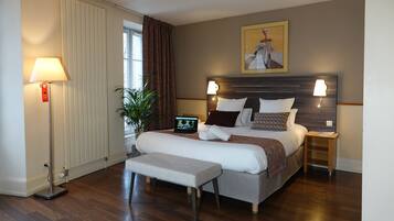 A modern hotel room with a large bed, bedside tables, a bench, a floor lamp, a potted plant, and a painting on the wall.