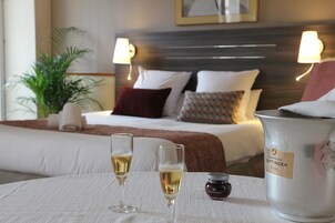 Une chambre d’hôtel avec un lit parfaitement fait, deux lampes de chevet, une bouteille de champagne et deux coupes de champagne posées sur une table.