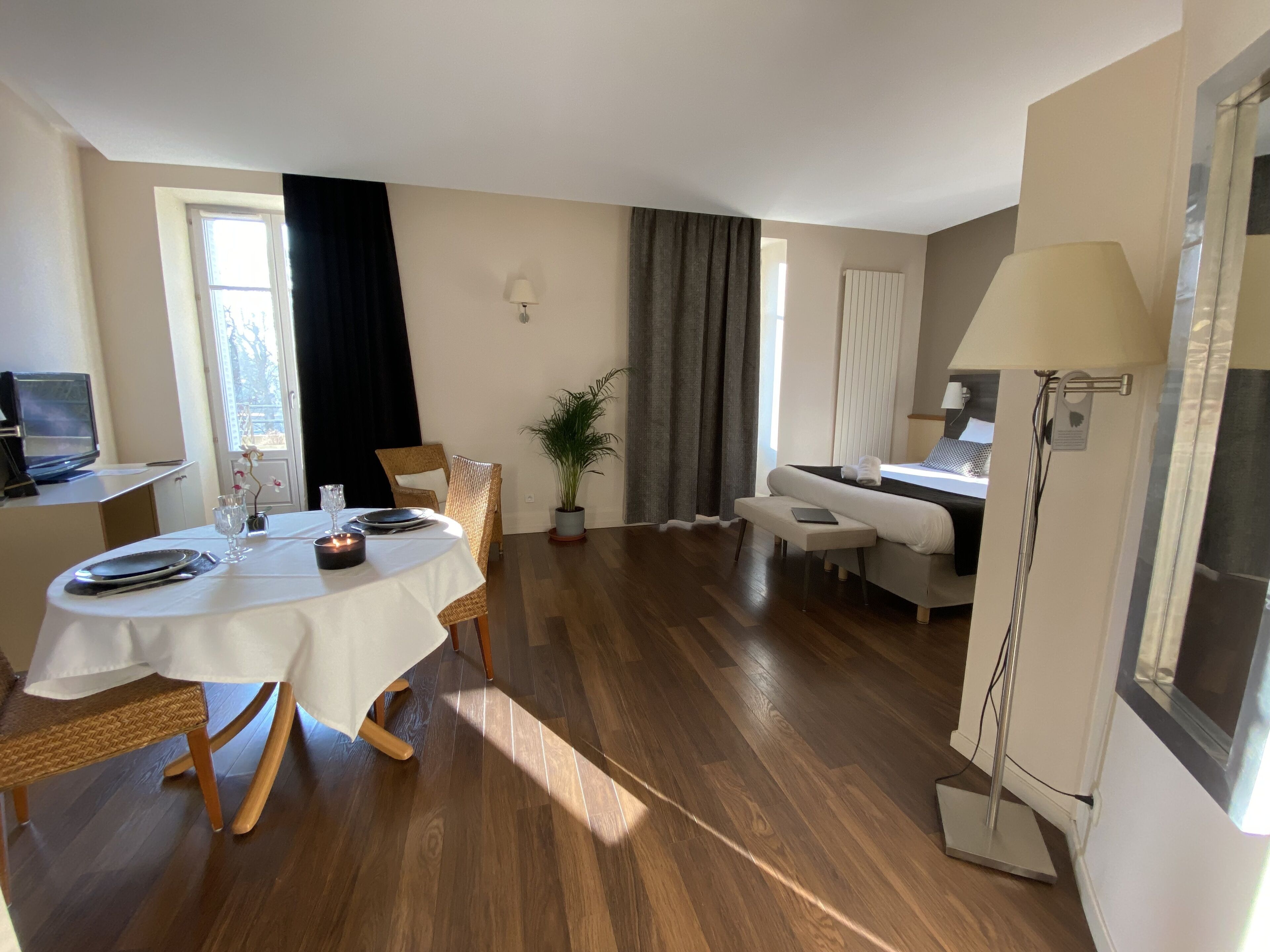 Una habitación de hotel con zona de comedor, cama, televisor y ducha.