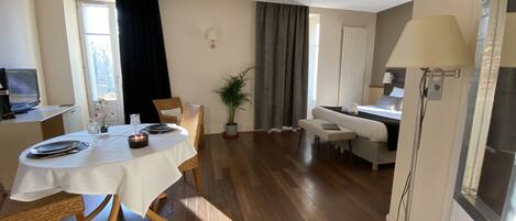 A hotel room with a dining area, a bed, a TV, and a shower.
