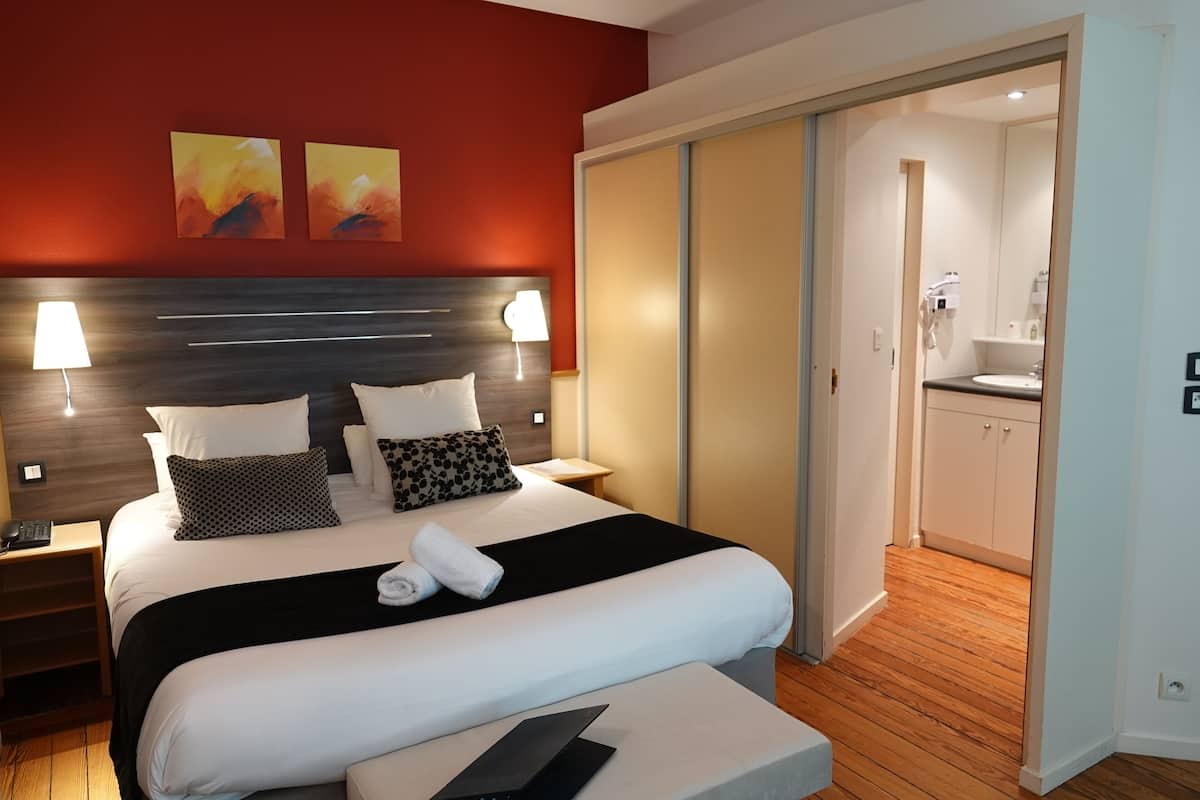 Een moderne hotelkamer met een groot bed, een nachtkastje met een lamp en uitzicht op de badkamer.