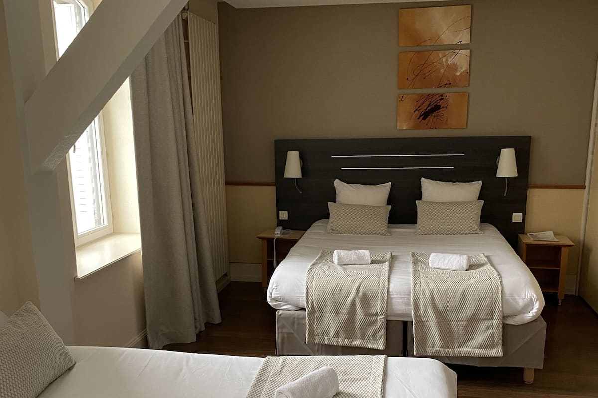 Een hotelkamer met twee bedden, een groot raam met gordijnen, een hoofdeinde met een lamp en een schilderij aan de muur.